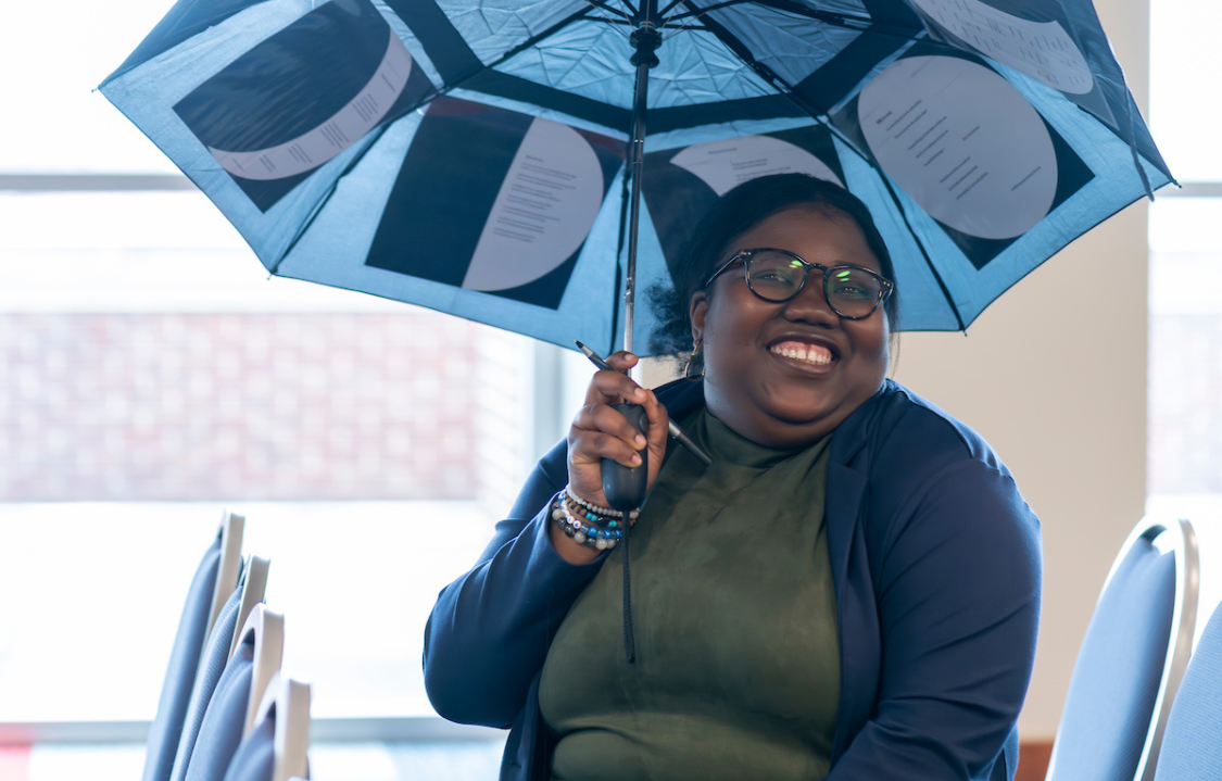 Student smiling and holding an umbrella.
